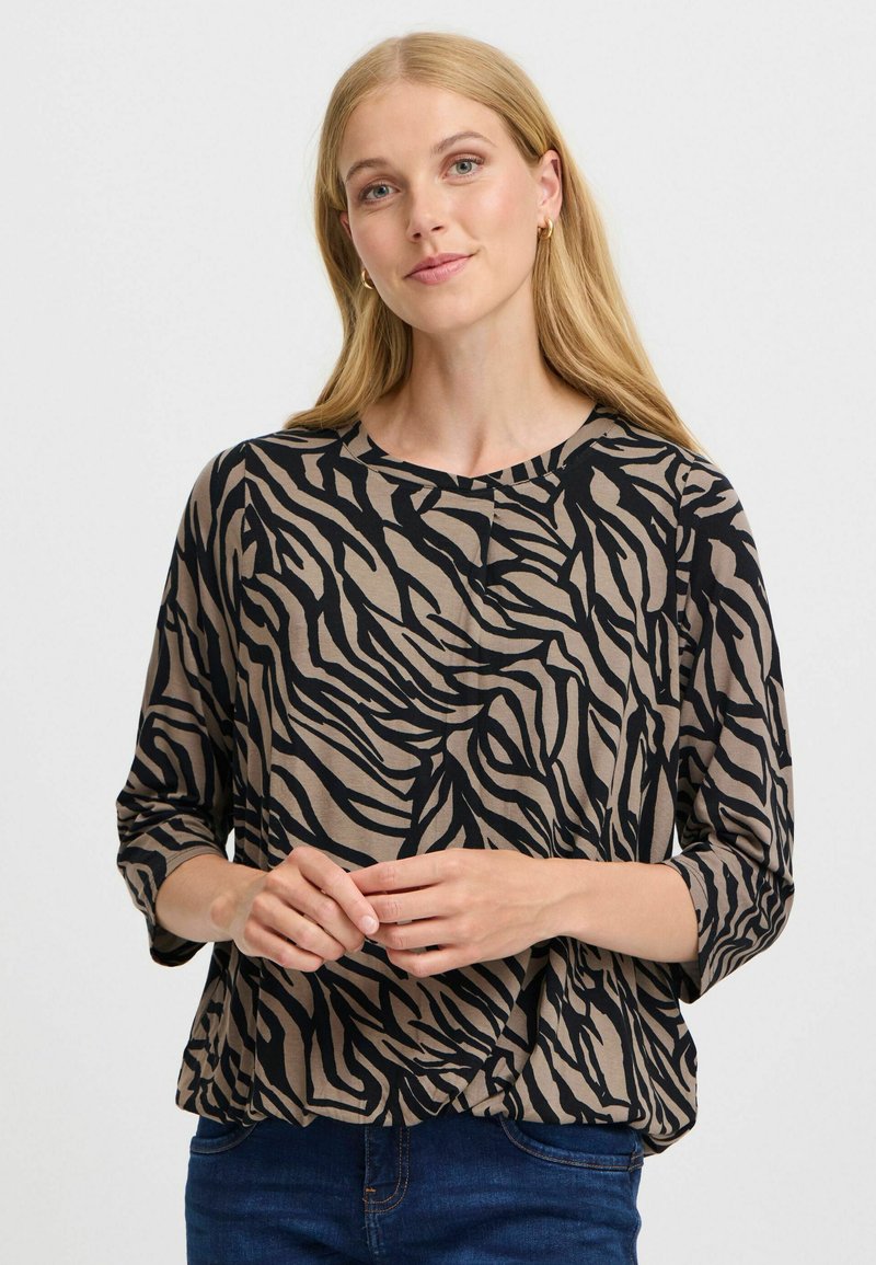 Beige topp med ett mönster av svarta zebraränder, avslappnad passform, rund halsringning och 3/4 ärmar. Tyget ser mjukt och lättviktigt ut.