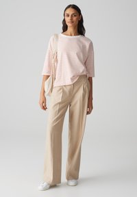 Gestreiftes T-Shirt in Rosa und Weiß, lockere Passform, kombiniert mit beigen High-Waist-Hosen, ergänzt durch weiße Sneaker und eine helle Tasche.