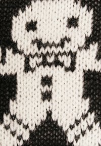 Schwarz-weißer gestrickter Stoff mit einem Charakterdesign, das Gesichtszüge und eine Fliege zeigt, und eine strukturierte, gemütliche Optik aufweist.
