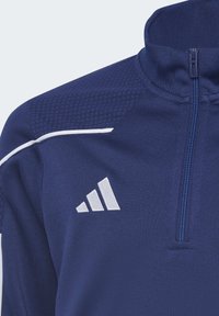Giacca sportiva blu navy con colletto alto, chiusura frontale con zip e pannelli sulle spalle testurizzati. Presenta accenti bianchi e un logo.