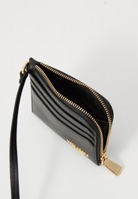 Black leather wallet with a gold zipper, featuring multiple card slots and a detachable wrist strap. Textured surface with gold hardware accents.