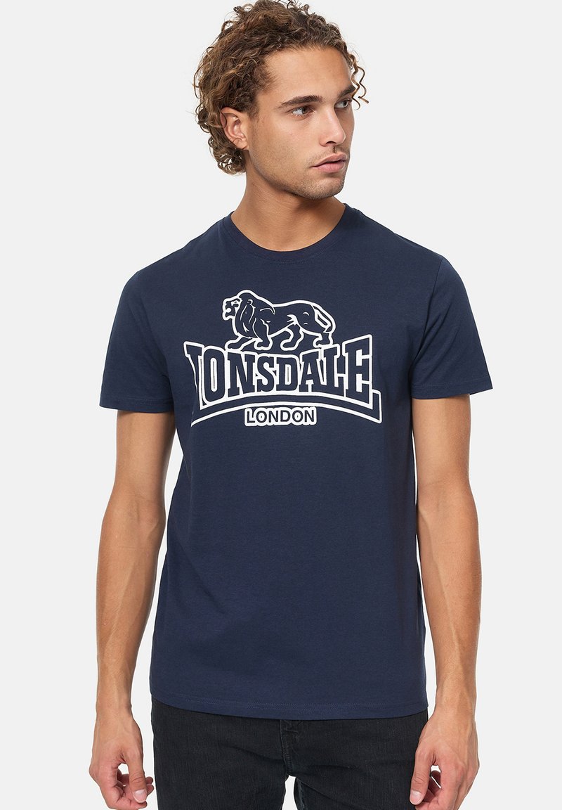 Sötétkék pamut póló, fehér oroszlán grafikával és "Lonsdale London" felirattal, kerek nyakkivágással és rövid ujjakkal.