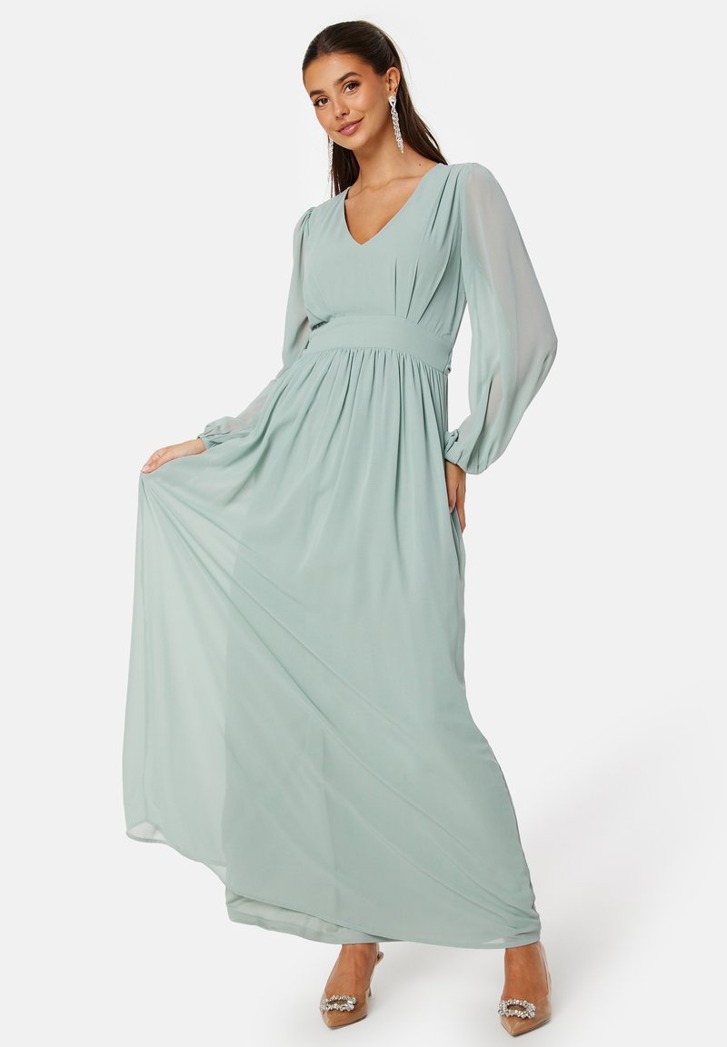 Een lange, mintgroene chiffon jurk met een V-halslijn, volumineuze mouwen, een empire taille en een vloeiende rok. Versterkt met een bijpassende riem.