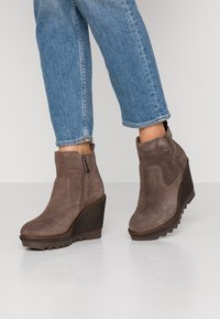 Bruna mockasin wedge ankelstövlar med en texturerad plattform, sidodragkedja och rund tå, paarade med ljusblå avskurna jeans.