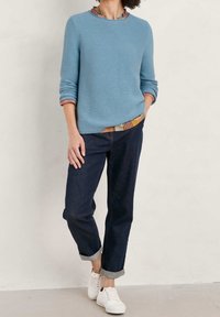 Lichtblauwe, geribbelde trui met ronde hals en opgerolde mouwen, gecombineerd met donkere denim jeans, omgeslagen bij de enkels, en witte sneakers.