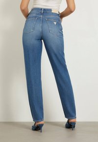 Jasnoniebieskie dżinsy o prostym kroju, z podwójnymi tylnymi kieszeniami i małym logo na pasku. Subtelna tekstura i wyblakłe wykończenie.