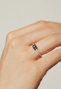 Anillo de plata que presenta tres piedras negras rectangulares en un diseño minimalista sobre una delicada banda con superficie texturizada.