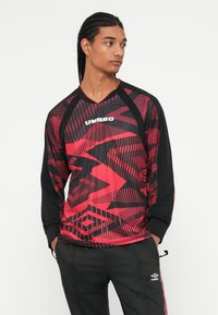 Rot und schwarz langärmliges Hemd mit geometrischen Mustern, Raglanärmeln und "UMBRO" Logo auf der Brust. Der Stoff wirkt leicht und glatt.