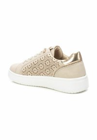 Zapatilla beige con un diseño floral perforado, acentos metálicos dorados en el talón y una suela de goma blanca. Parte delantera con cordones texturizados.