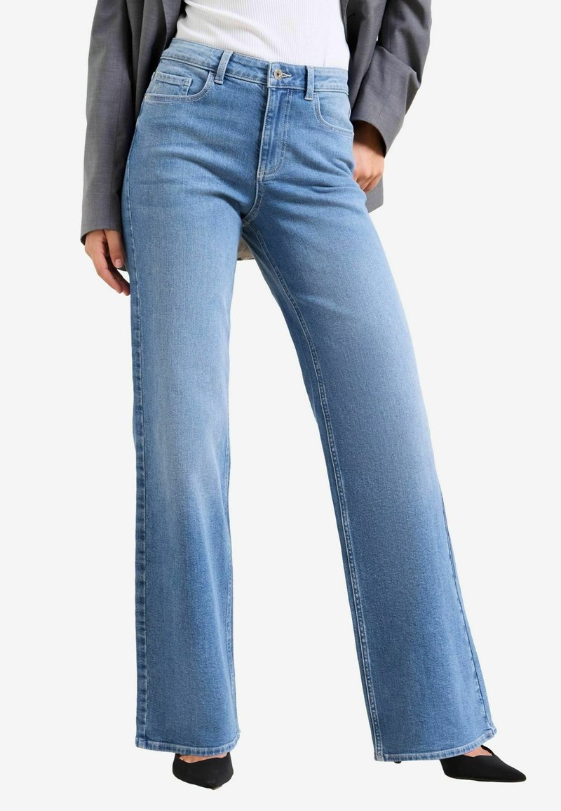 Gaiši zili džinsa platā stila bikses ar augstu jostasvietu, priekšējiem kabatām un tīru apdari apakšmalā, apvienotas ar melnu apavu papēdi.