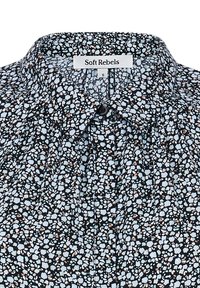 Bunte Bluse mit schwarzem Hintergrund und hellblauen sowie beigen Blumenmustern. Mit Kragen, Knopfdetails und weichem Material.