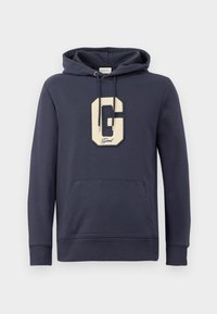 Marineblå hættetrøje lavet af en bomuldsblanding, prydet med et stort cremefarvet "G" logo med broderi og en frontlomme.