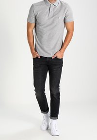 Grå polo-shirt med krave, parret med mørke jeans og hvide sneakers. Bemærkelsesværdig logo-detalje på venstre bryst.