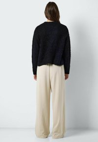 Zwarte, fuzzy sweater met een ronde hals en een relaxed fit, gecombineerd met losse, off-white broeken. De stof heeft een zachte textuur.