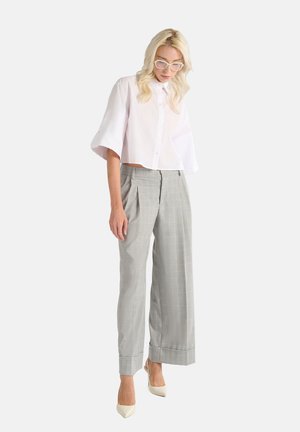 Chemise blanche raccourcie à boutons avec des manches larges, associée à un pantalon large à carreaux gris taille haute et des escarpins beige à bout pointu.