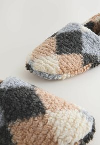 Fuzzy, wsuwane kapcie mają wzór w patchworku w kolorach beżowym, taupe, szarym i czarnym, z miękką teksturowaną powierzchnią.
