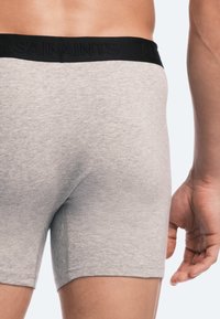 Gray cotton boxer briefs with a black elastic waistband featuring embossed text. Close-up, showing side and back design details.