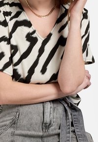 Top a maniche corte con scollatura a V in crema con strisce astratte nere. Tessuto morbido e vestibilità ampia, abbinato a pantaloni corti in denim grigi a vita alta.