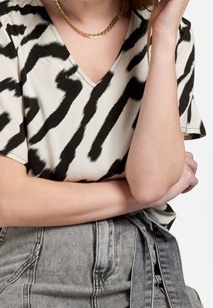 Top a maniche corte con scollatura a V in crema con strisce astratte nere. Tessuto morbido e vestibilità ampia, abbinato a pantaloni corti in denim grigi a vita alta.