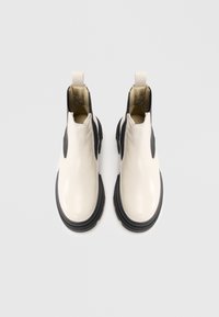 Pár lesklých off-white kotníkových bot s černými elastickými bočními panely a masivními černými podrážkami viděných shora.