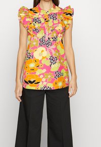 Colorful floral blouse with pink base, ruffled neckline, and short sleeves. Features large orange and yellow flowers complemented by black accents.