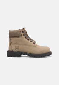 Stivaletto alla caviglia in suede marrone chiaro con collo imbottito, occhielli in metallo, lacci marroni e suola in gomma nera con un motivo scolpito. Logo Timberland impresso.