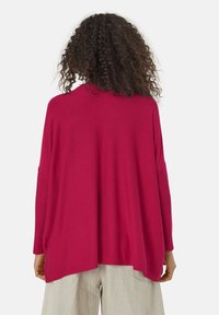 Pull oversized fuchsia avec des manches longues, texture côtelée aux poignets et à l'ourlet, offre une coupe décontractée et des fentes sur les côtés pour plus de liberté de mouvement.