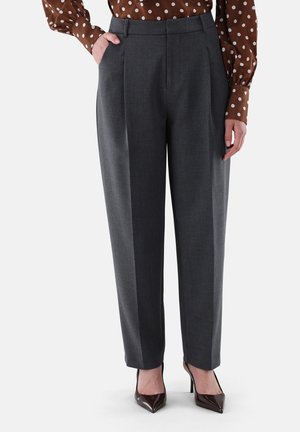 Woman wearing dark gray tailored trousers with a pleat, paired with brown polka dot blouse and dark pointed high heels.