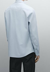 Camicia azzurra a maniche lunghe con colletto abbottonato, caratterizzata da una trama liscia e un orlo curvo, abbinata a pantaloni in denim scuro.