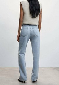 Jeans de tiro alto en un azul claro con un corte recto, que cuentan con dos bolsillos traseros y una textura ligeramente desgastada. Se combinan con una blusa de punto en tonos neutros.