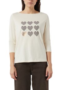 Kremowa koszula z długim rękawem i okrągłym dekoltem, na przodzie dziewięć wzorów serc w czarno-złote paski. Miękki, gładki bawełniany materiał.