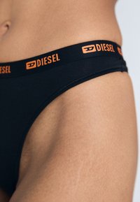 Culotte de bikini en coton noir avec une taille élastique portant l'inscription "DIESEL" en lettres orange. Texture lisse avec un ajustement près du corps.