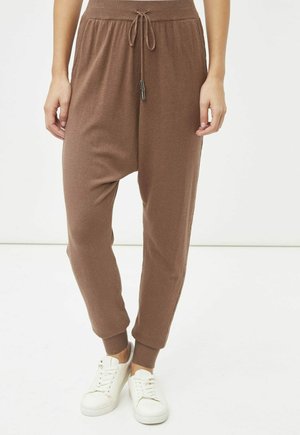 Pantalones harem marrones de tejido suave, con cintura ajustable, puños elásticos y un corte relajado. Combinados con zapatillas blancas.