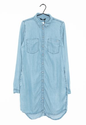 Hellblaues Jeanskleid mit langen Ärmeln, Kragen, vorderen Knöpfen, zwei Brusttaschen und abgerundetem Saum, das an einem schwarzen Kleiderbügel hängt.