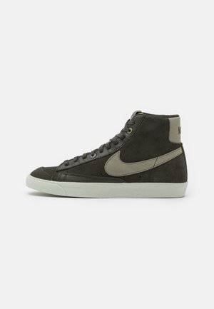 Baskets montantes noires en daim avec le swoosh beige de Nike et une semelle en caoutchouc blanche, lacets sur le devant et col matelassé à la cheville.