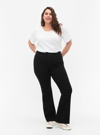 Black flared pants with five pockets and a smooth texture, paired with a plain white short-sleeve T-shirt. Model stands confidently.