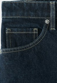 Poche de jean en denim bleu foncé avec des coutures beiges contrastées et un petit rivet métallique dans le coin supérieur.