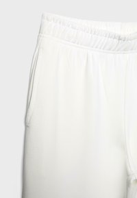 Pantalon de survêtement à taille élastique blanche avec poches latérales, présenté en gros plan sur un fond clair uni.