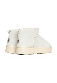 Stivaletti alla caviglia color crema realizzati in morbido suede, con fodera soffice e suola in gomma spessa; presentano accenti con logo e dettagli di cucitura minimal.
