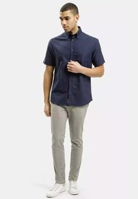 Granatowa koszula krótki rękaw zapinana na guziki z kieszonką na piersi, zestawiona z jasnoszarymi dopasowanymi spodniami i białymi trampkami. Prosty design i gładka tekstura.