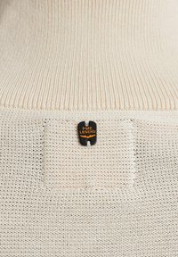 Beżowy sweter z dzianiny z żebrowanym kołnierzem oraz czarną metką z napisem "PME LEGEND" w kolorze pomarańczowym. Charakteryzuje się delikatną fakturą i prostym designem.
