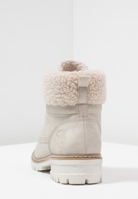 Beige suède enkellaars met een fluffige crèmekleurige kraag, rubberen zool en versterkte stiksels, voorzien van een trekkoord voor gemakkelijk aan- en uittrekken.