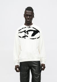 Λευκή μπλούζα μελανζέ με μαύρο αφηρημένο γραφικό μπροστά, στρογγυλή λαιμόκοψη και ριμπ μανσέτες, σε συνδυασμό με μαύρο δερμάτινο παντελόνι cargo.