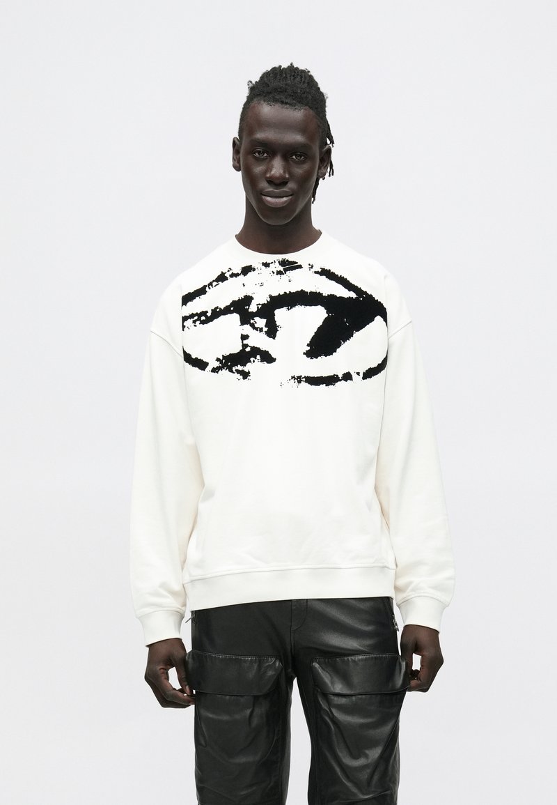 Λευκή μπλούζα μελανζέ με μαύρο αφηρημένο γραφικό μπροστά, στρογγυλή λαιμόκοψη και ριμπ μανσέτες, σε συνδυασμό με μαύρο δερμάτινο παντελόνι cargo.