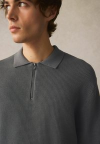 Grå zip-up polo t-shirt med et struktureret mønster, der har krave og en halv længde lynlås, tætsiddende design med blødt stof.
