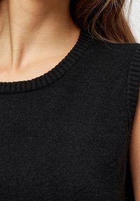 Top senza maniche lavorato a maglia nera con scollatura rotonda a costine, caratterizzato da una texture morbida e un design aderente. Nessun motivo o accessorio visibile.