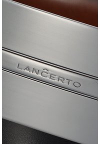 Metaliczny srebrny pasek z wygrawerowanym logo "LANCERTO". Gładka tekstura, dwie równoległe linie oraz elegancki design. Brązowe tło z skóry.