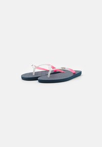 Des tongs avec une semelle en bleu marine texturée, des brides transparentes blanches et roses, et un accent de logo argenté sur la bride.