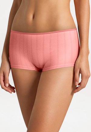 Femme portant un shorty côtelé rose, visible de la taille aux cuisses sur un fond uni.