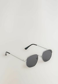 Gafas de sol de metal plateado con lentes oscuros redondos, con varillas delgadas con puntas negras y un diseño minimalista.